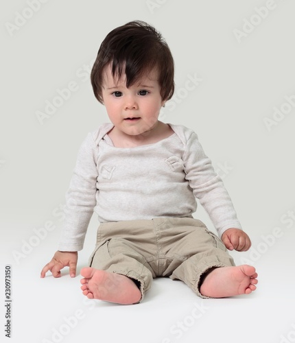 Funny baby sitting on the floor, isolated over white