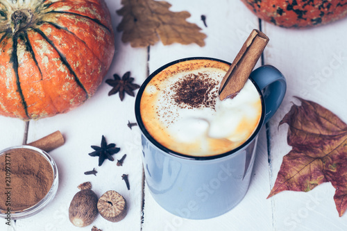 Pumpkin spice latte or coffee with cinnamon and nutmeg. Autumn, fall or winter hot drink. Old white wooden background with yellow leaves and pumpkins photo