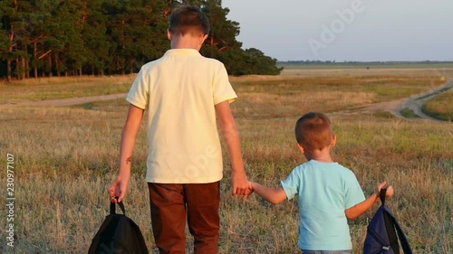 Two boys walking with backpacks at sunset. Happy children walk by nature, near the forest. photo