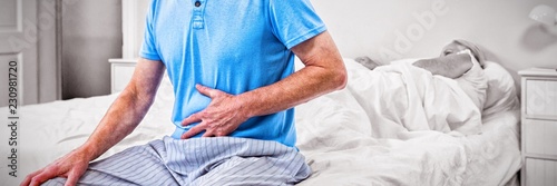 Foto Senior man having stomach pain while sitting on bed