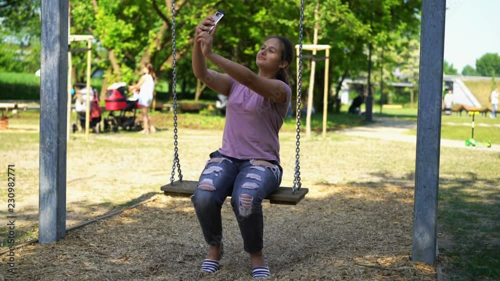 Teenage girl taking selfie photo on swing in city park Teenage girl taking selfie photo on swing in city park