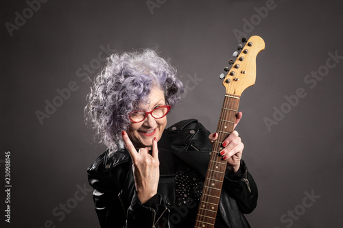 Close up portrait of beautiful older woman holding an electric guitar on a gray background