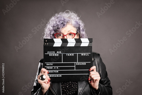 Close up portrait of beautiful older woman holding a movie clapper on a gray background