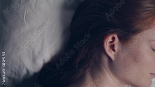 Nighttime top view revealing shot of a young woman sleeping alone in bed.