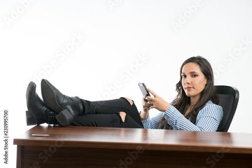 Woman with smartphone, texting in the office, sitting with legs on desk