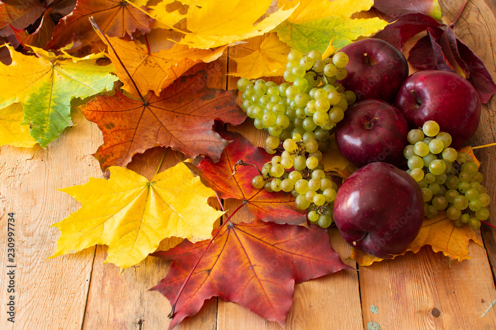 Red Juicy Ripe Apples with Green Grapes and Autumn Maple Leaves on a Wooden Background Red Juicy Ripe Apples with Green Grapes and Autumn Maple Leaves on a Wooden Background