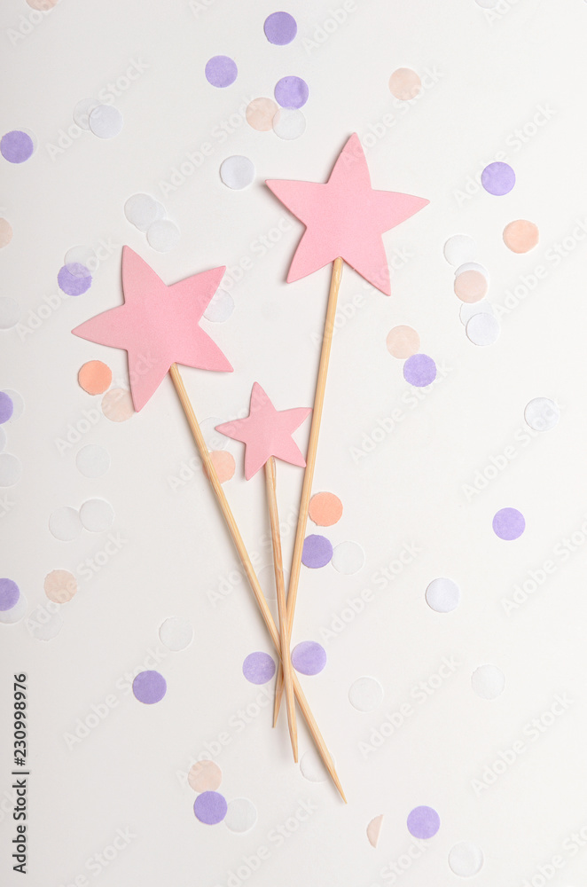 Pink stars on a stick topping on white background with confetti, pastel colors. Children's holiday, new year. Top view, flat lay