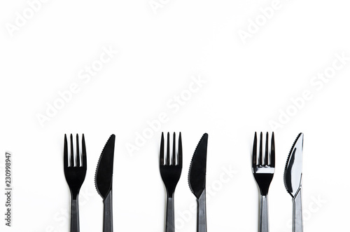 Clean plastic black forks and knives on white background. Disposable dishes  environmental pollution. Copy space  top view  flat lay.