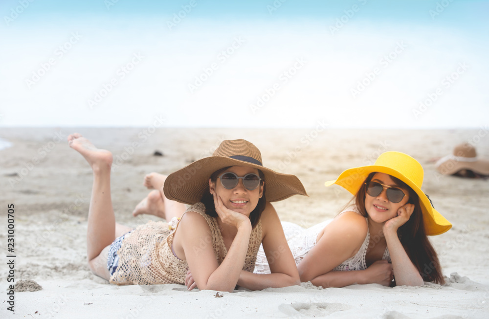 Two women happily lie on the beach.