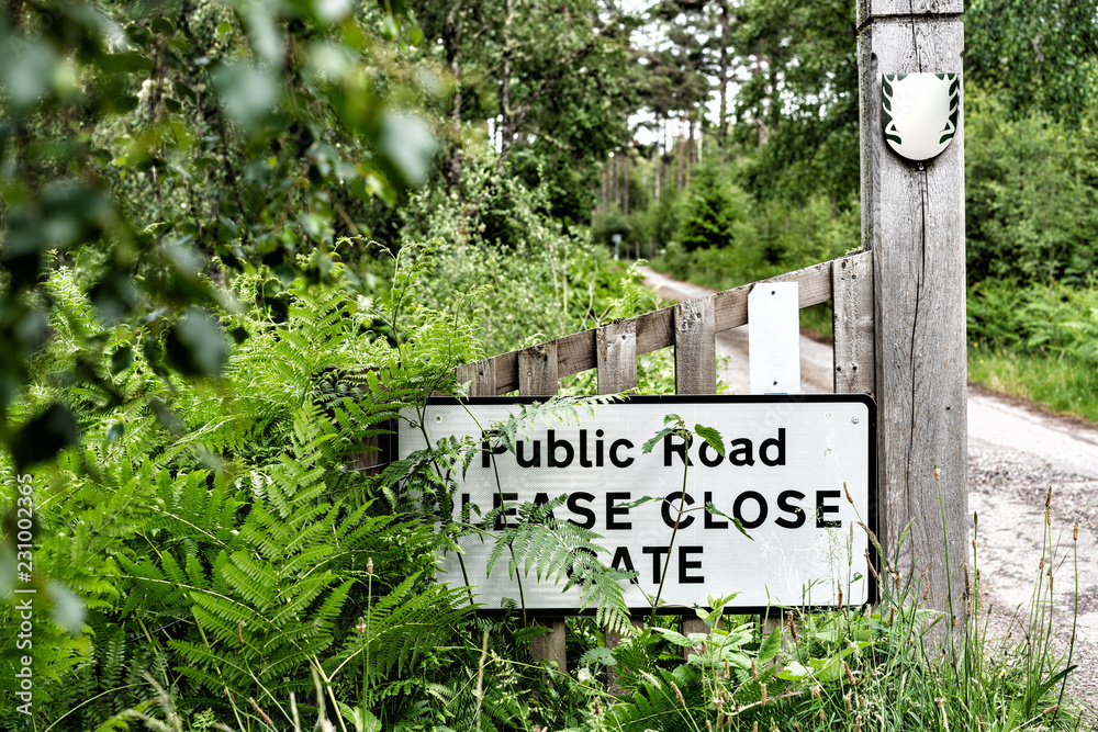 © Petra - Offenes Holztor an der Seite ein Schild befestigt worauf steht Public Road PLEASE CLOSE GATE dahinter Wald und Natur