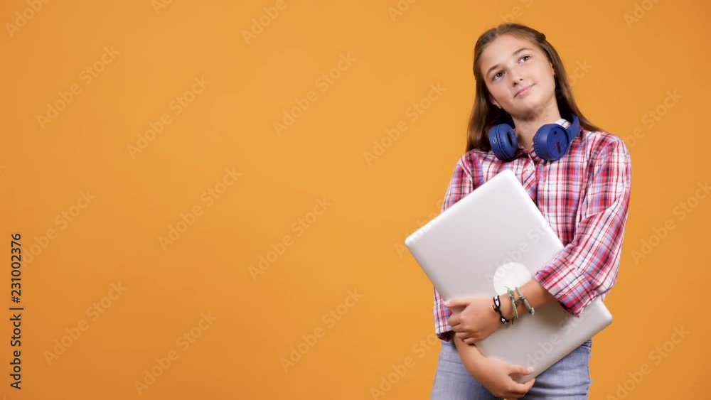 Young girl holding a laptop in hands isolated over orange yellow background in studio Young girl holding a laptop in hands isolated over orange yellow background in studio