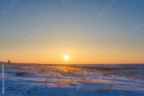 Winter landscape with snow covered plain, blue sky and orange su