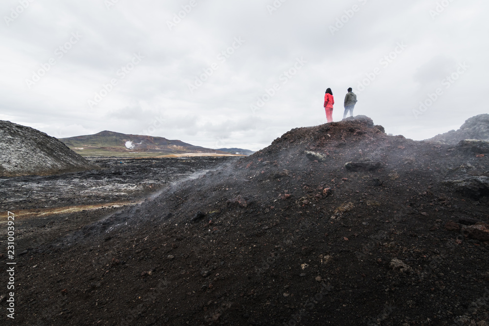 Woman and man figures standing in Krafla volcano lava field around Leirhnjukur mountain peak, Iceland
