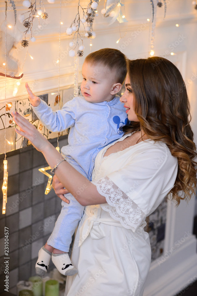 Fototapeta premium Merry Christmas celebration. Beautiful mom and little son at home near the Christmas tree. Christmas miracles.