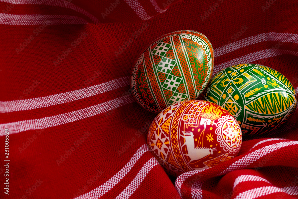 Spring holiday and happy easter concept with three dyed eggs in a rustic vintage red cloth with each egg having different complex and intricate pattern specific to eastern europe with copy space