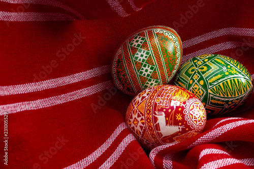 Obraz na płótnie Spring holiday and happy easter concept with three dyed eggs in a rustic vintage red cloth with each egg having different complex and intricate pattern specific to eastern europe with copy space w salonie
