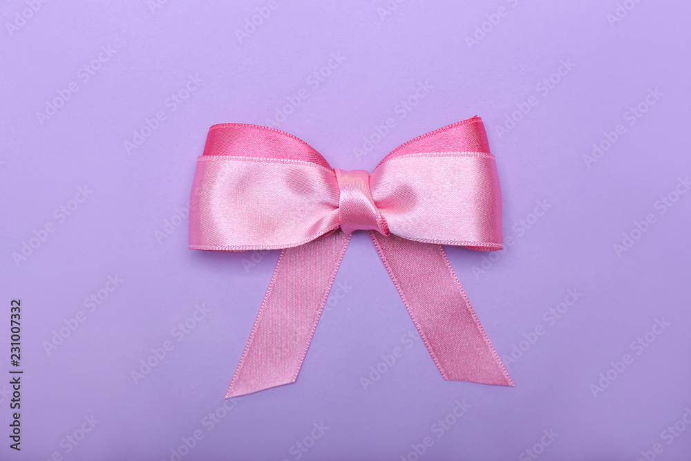 Beautiful bow made of pink ribbon on color background
