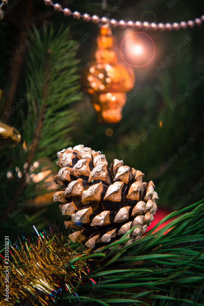 Fototapeta premium Spruce branch with cone and balls, festive lights on the background.