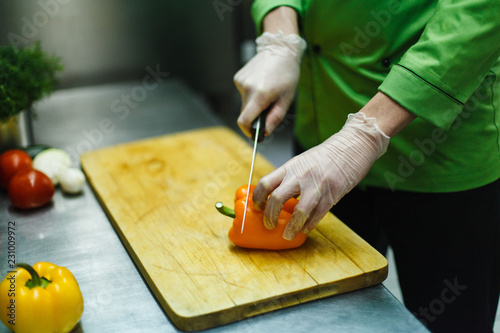 cook in gloves cuts vegetables on a wooden board. professional kitchen with steel worktop