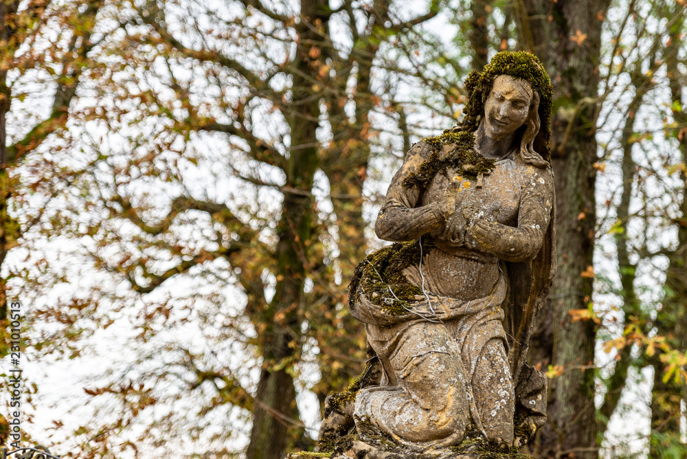 Statue religieuse sans mains couverte de mousse d'un cimetière en Moselle
