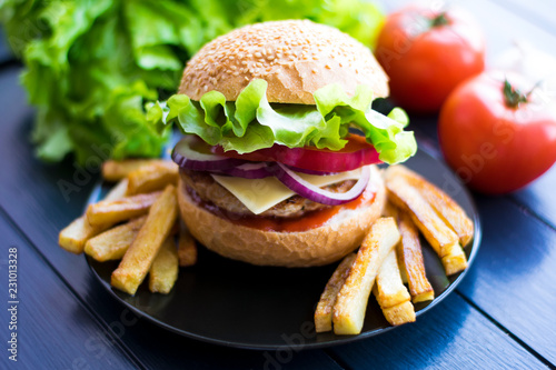 Tasty fresh closeup burger and french fries on wooden table. Homemade hamburger with fresh vegetables.