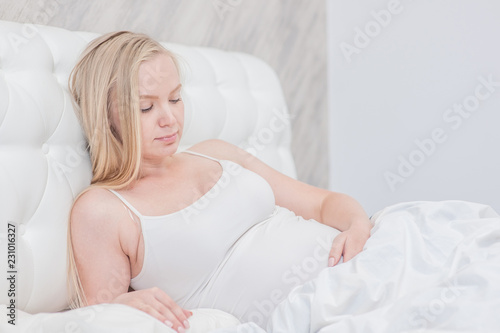 Beautiful pregnant woman on the bed looking on the belly