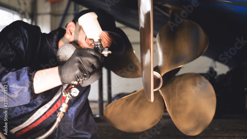 The yacht technician cleans the propeller using a chemical spray (paint) cleaner from dirt. Concept from: New technique, Chemistry, Profesional, Paint, Respirator, Mask, Yacht Club.  © dkHDvideo