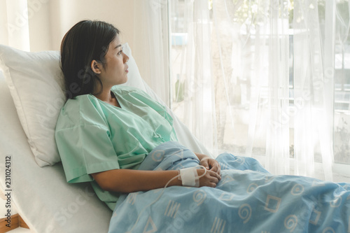 young woman sitting on the bed and looking outside window in hospital worry about her illness.