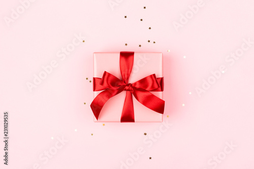 Pink gift box with red bow on the pink background with sparkles. Holiday conc...