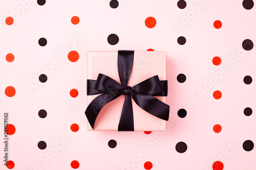 Pink gift box with black bow on pink background with red and black polka dots...