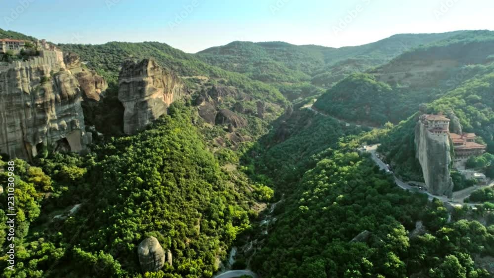 Back moving aerial shot of wonderful natural valley with high mountains and dense green trees at sunset rock Meteora with monasteries on peak of cliff tourist historical place in Greece Back moving aerial shot of wonderful natural valley with high mountains and dense green trees at sunset rock Meteora with monasteries on peak of cliff tourist historical place in Greece