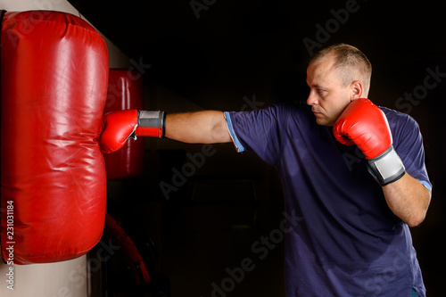 novice male boxer training with punching bag on dark background.