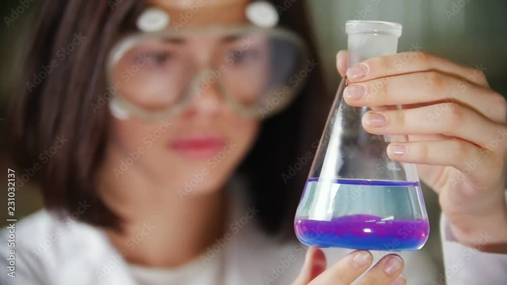 Young woman in chemical laboratory holding a flask with blue and purple liquid.Focus on the flask. Young woman in chemical laboratory holding a flask with blue and purple liquid.Focus on the flask.