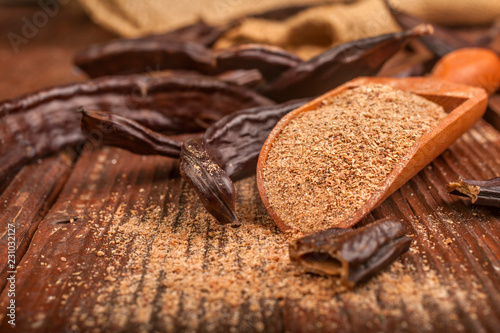 Carob pods and carob powder in a spoon on rustic background
