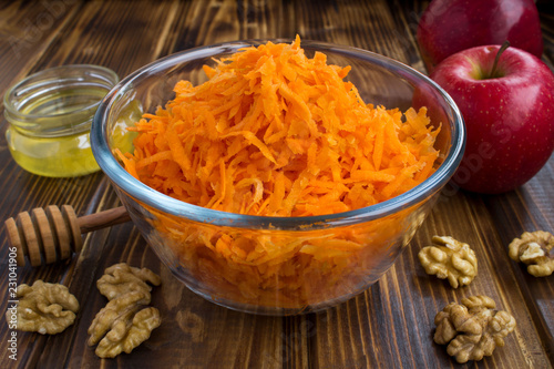 Grated carrot in the glass bowl and ingredients for salad on the brown wooden  background