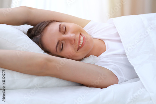 Beautiful young and happy woman stretching hands while lying in bed comfortably and blissfully smiling befor wake up in a morning. Sleeping concept