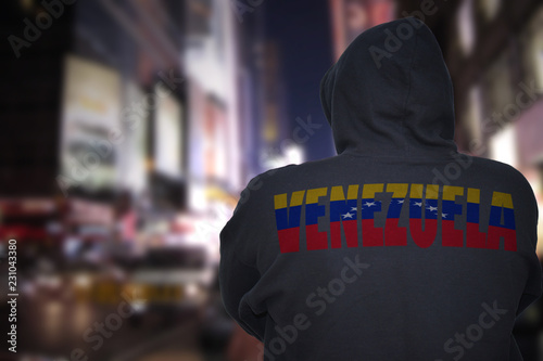 dangerous man standing on a city street with black hoodie with text venezuela on his back © luzitanija
