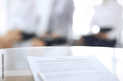 Contract with a pen and blurred business people on the background, close-up. Female candidates waiting for interview at queue