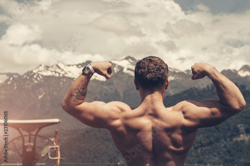 Young bodybuilder showing muscles shape outdoors, Handsome muscular bearded man looking at highlands landscape with foggy sky from the peak of the mountain, feeling hapyness and joy. photo
