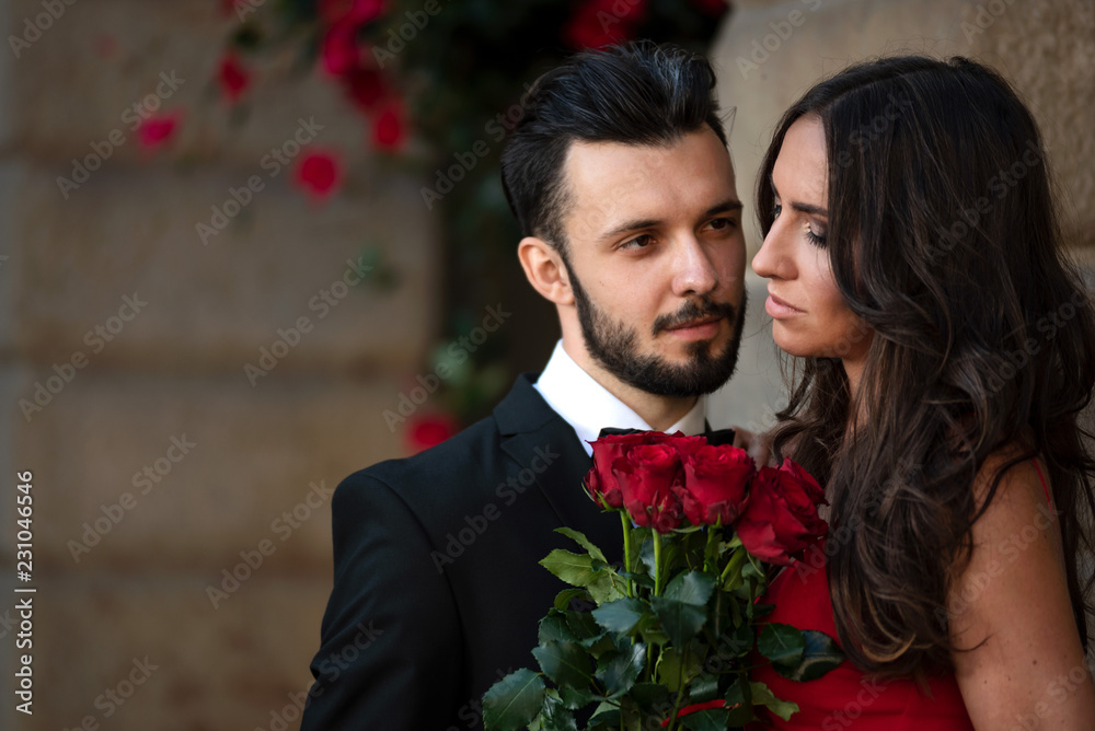 Portrait of an elegant fashion couple in love on a romantic date. Man giving a bouquet of red roses to a woman. v Portrait of an elegant fashion couple in love on a romantic date. Man giving a bouquet of red roses to a woman. v