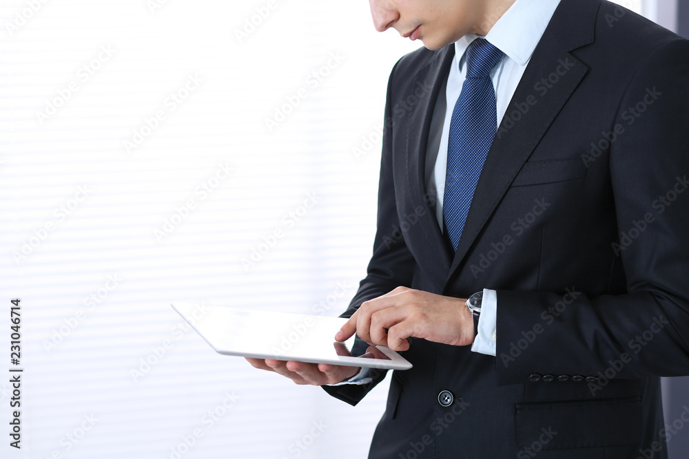 Young businessman using tablet computer while standing straight in office. Business concept Young businessman using tablet computer while standing straight in office. Business concept