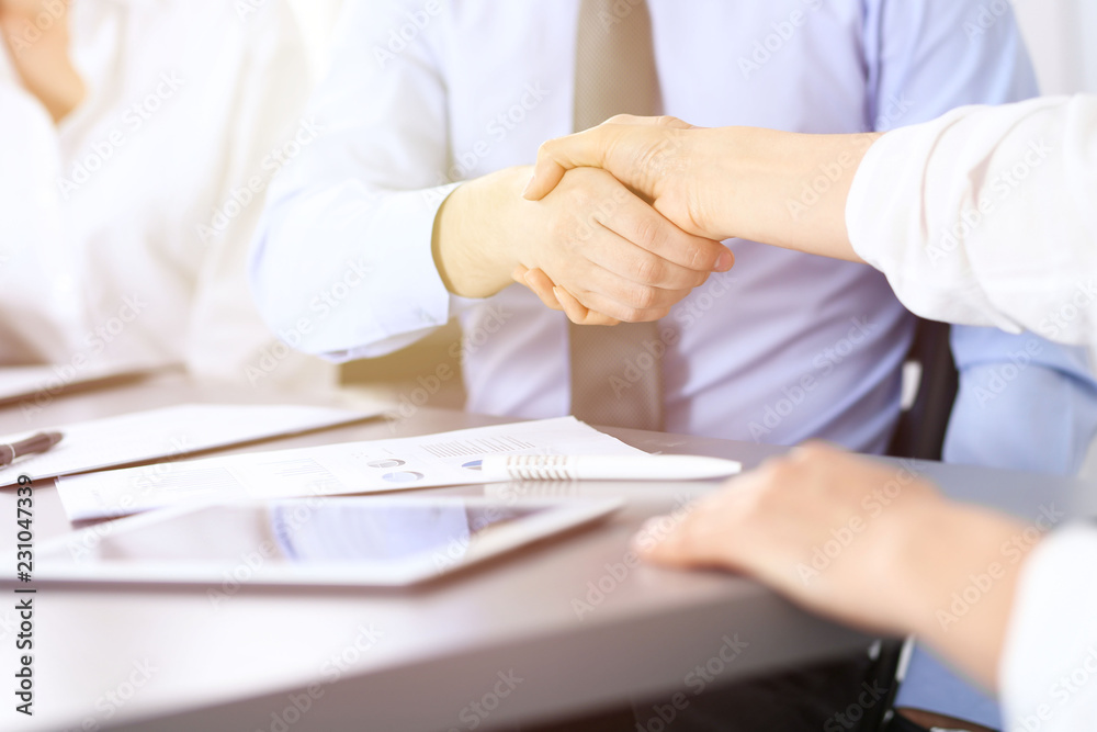 Close-up of business handshake at meeting or negotiation above the desk in office. Partners shaking hands while satisfied because signing contract or financial papers. Success concept Close-up of business handshake at meeting or negotiation above the desk in office. Partners shaking hands while satisfied because signing contract or financial papers. Success concept