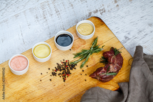 cut off beef with herbs and sauces on a wooden board.