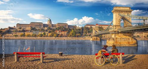 A couple enjoying the view while sitting on a bench near the Danube river embankment in Budapest, Hungary.