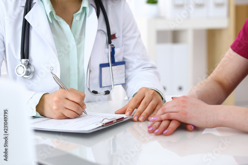 Doctor woman consulting patient while filling up an application form at the desk in hospital. Just hands close-up. Medicine and health care concept