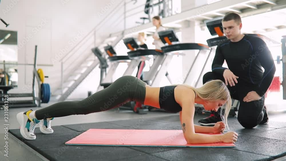 Fitness instructor control how woman make plank exercise in gym