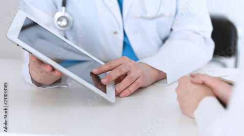  Closeup of a doctor and patient sitting at the desk. Physician pointing into tablet pc. Medicine and health care concept