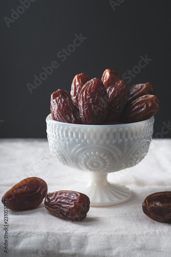 Bowl of medjool dates in a white bowl with side lighting.