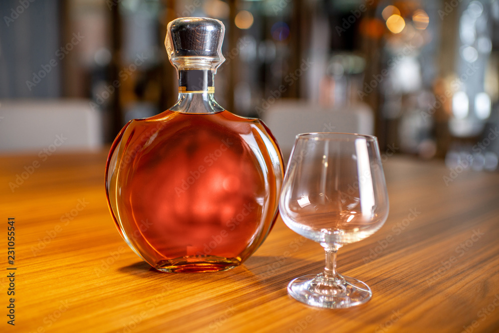 Bottle of the cognac with empty glass on the table in cigar room Bottle of the cognac with empty glass on the table in cigar room