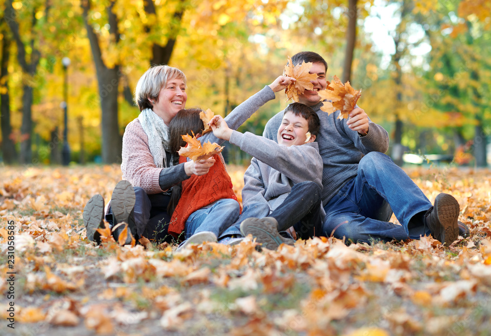 Happy family sit in autumn city park on fallen leaves. Children and parents posing, smiling, playing and having fun. Bright yellow trees. Happy family sit in autumn city park on fallen leaves. Children and parents posing, smiling, playing and having fun. Bright yellow trees.